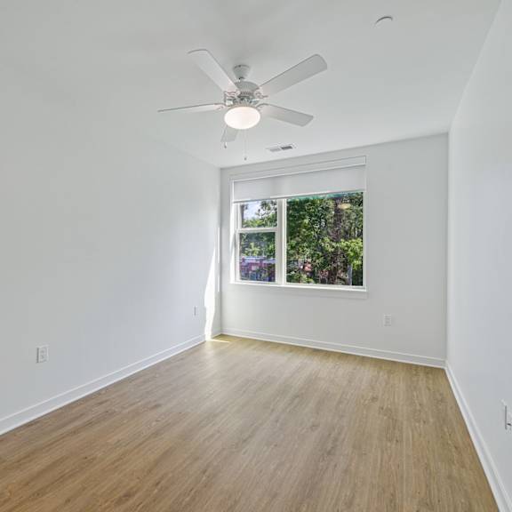 a room with a ceiling fan and a window with a view of trees.
