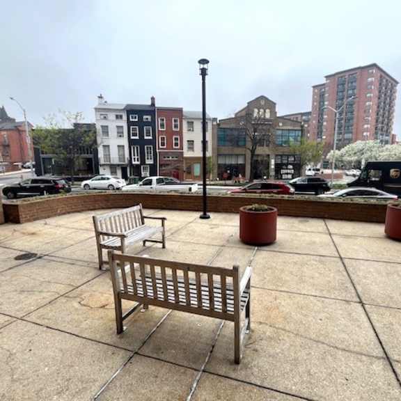 a bench sits on a paved area with a building in the background.