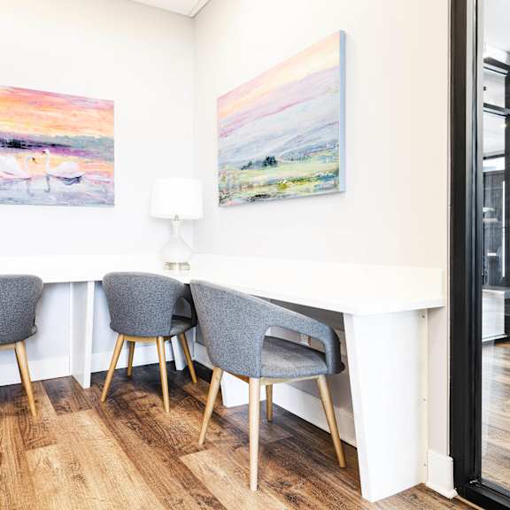 a home office with two paintings on the wall and a white table with three gray chairs