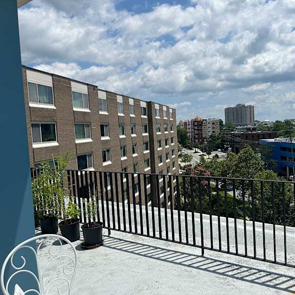 a balcony with a black railing and potted plants overlooks a cityscape.