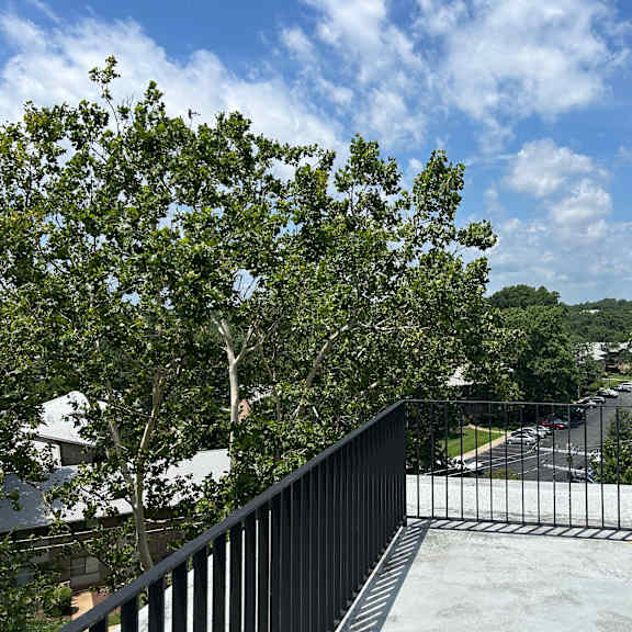 a balcony with a black railing overlooks a street with cars and houses.