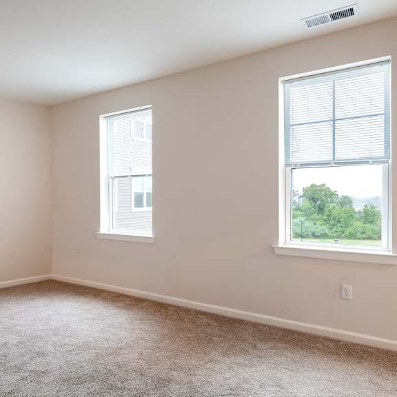 an empty bedroom with two windows and carpeting