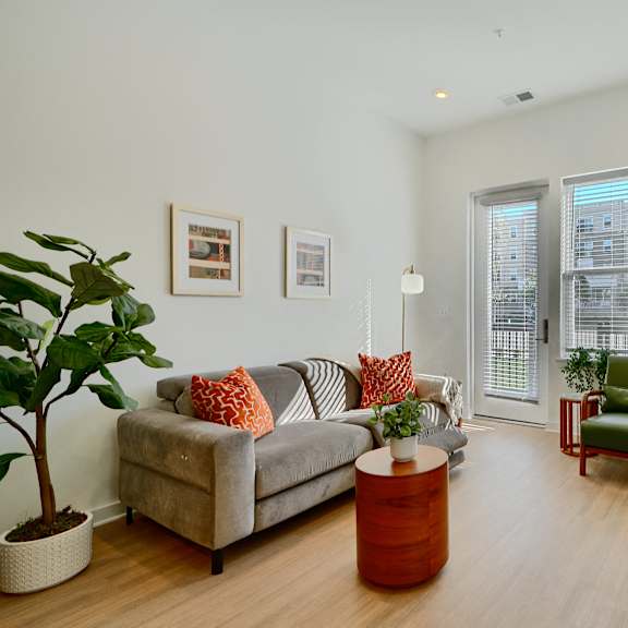 now leasing senior 1-bedrooms in baltimore, md. a living room with a grey couch and a green chair.