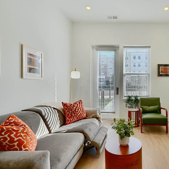 now leasing senior 1-bedrooms in baltimore, md. a living room with a grey couch, a green chair, and a green bookshelf.