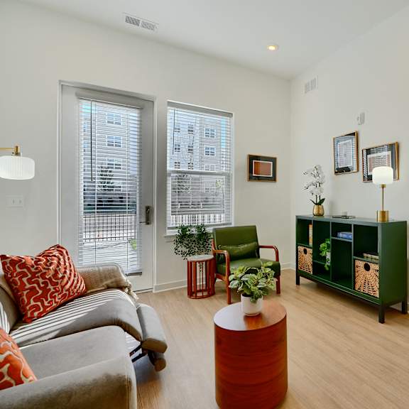 now leasing senior 1-bedrooms in baltimore, md. a living room with a grey couch and a red pillow.