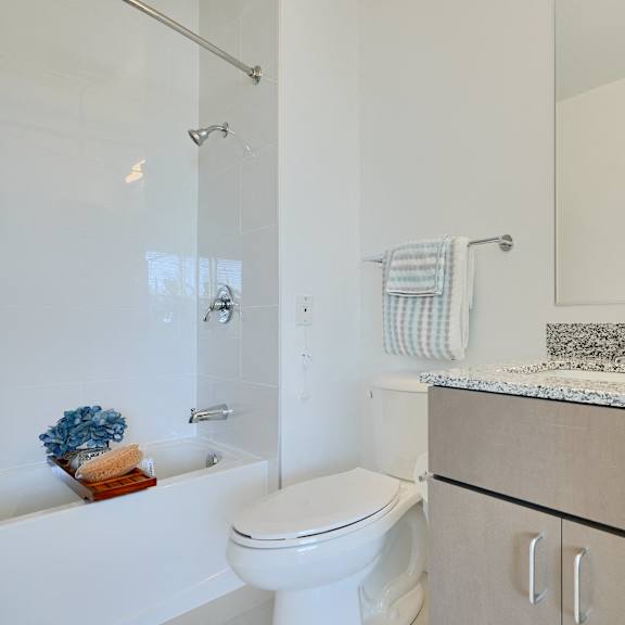 now leasing senior 1-bedrooms in baltimore, md. a white toilet sits in a bathroom with a white tub and a white sink.