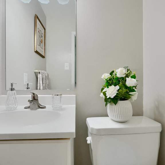 a white toilet sits next to a sink with a vase of flowers on top.