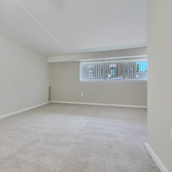 a spacious, empty room with a carpeted floor and a window with blinds.