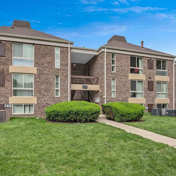 a brick apartment building with green grass and a sidewalk