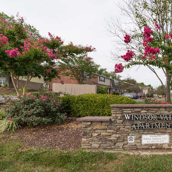 a sign for windsor valley apartments is surrounded by flowers and greenery.