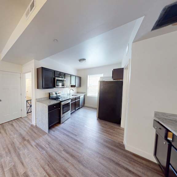 a kitchen with a black fridge and a wooden floor.