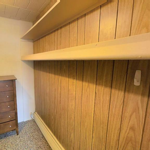 a wooden dresser sits in a room with a white wall and a wooden shelf above it.
