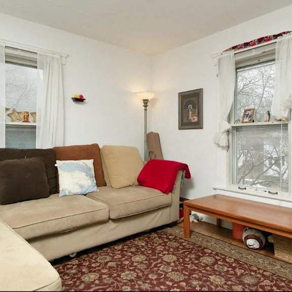 a living room with a beige couch, a small table, and a window with white curtains.