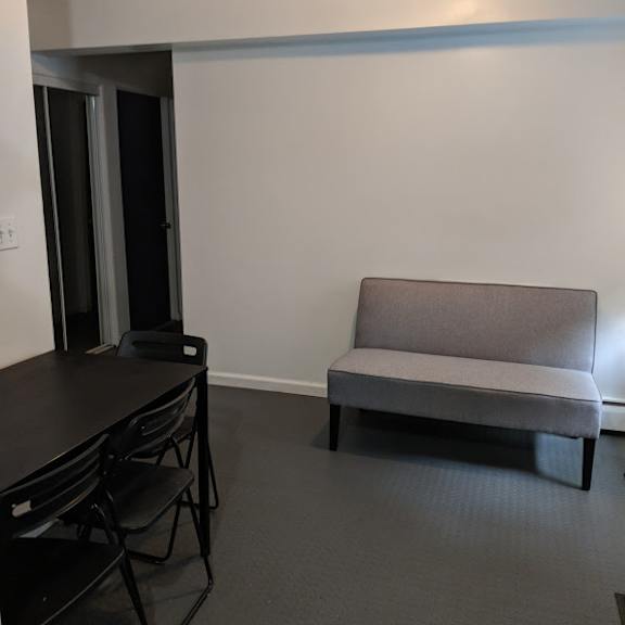a grey sofa sits in a room with a black table and chairs.