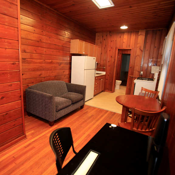 a small room with a couch, chair, table and a refrigerator.