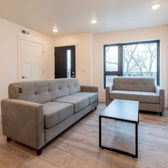 a grey couch and a grey chair are in a room with a window.
