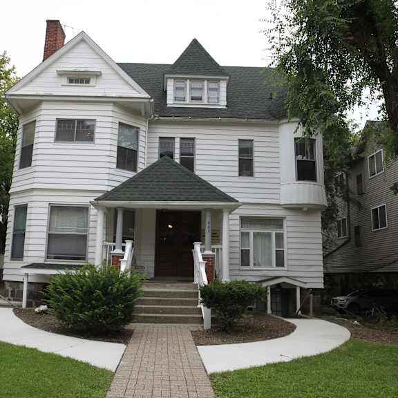 a white victorian style house with a black roof and a brick walkway leading to the front door.