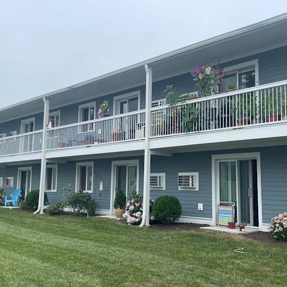 a blue building with a balcony and a grass field