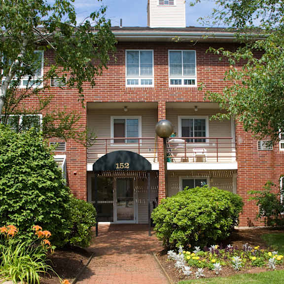 the front of a red brick apartment building with a sidewalk and trees