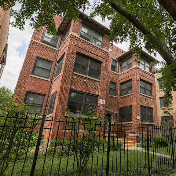 a red brick building with a black fence and trees in front.
