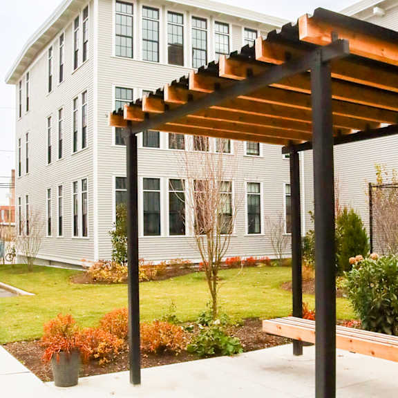 a bench under a pergola with a white building behind it