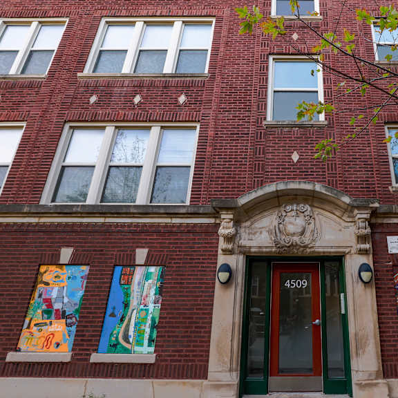 a red brick building with a green door and three colorful paintings on the wall.