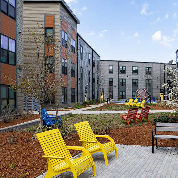 a playground area with a bench, chairs and a slide in front of apartment buildings.