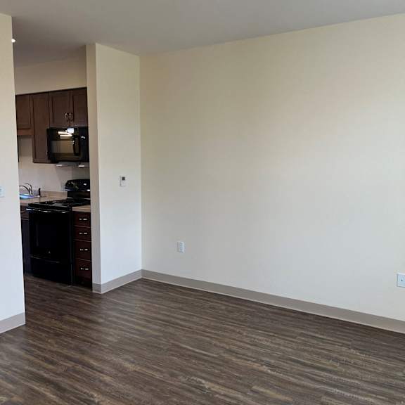 an empty living room with wood flooring and a kitchen