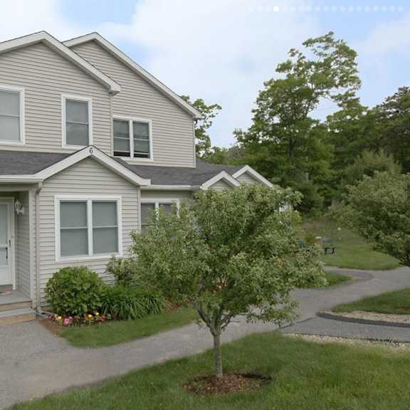 a house with a grey roof and white walls with a small tree in front of it.