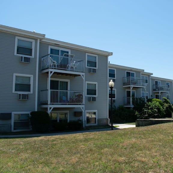 a row of grey apartment buildings with balconies and a grassy area in front of them