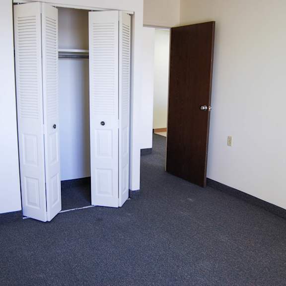 a room with a carpeted floor and a white door with a shelf.