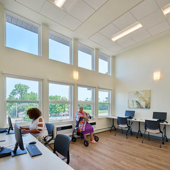 a woman is sitting at a desk in a room with large windows.