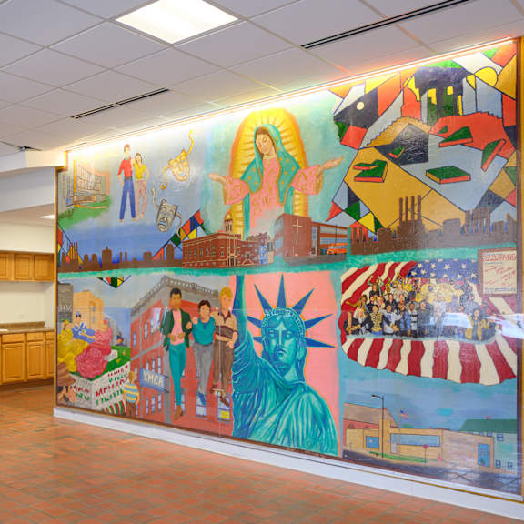 a group of people are sitting and standing in a room with a large mural on the wall.