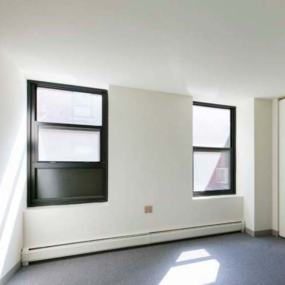 a room with white walls and a grey floor with a row of cupboards on the right.