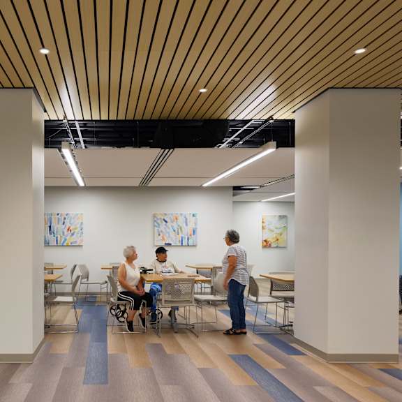 a group of people are sitting and standing in a room with wooden floors and ceiling.