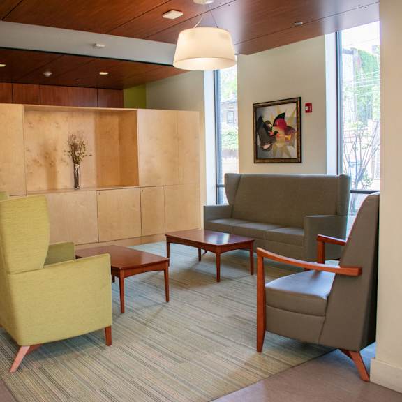 a seating area with chairs and tables in front of a wall with a painting on it