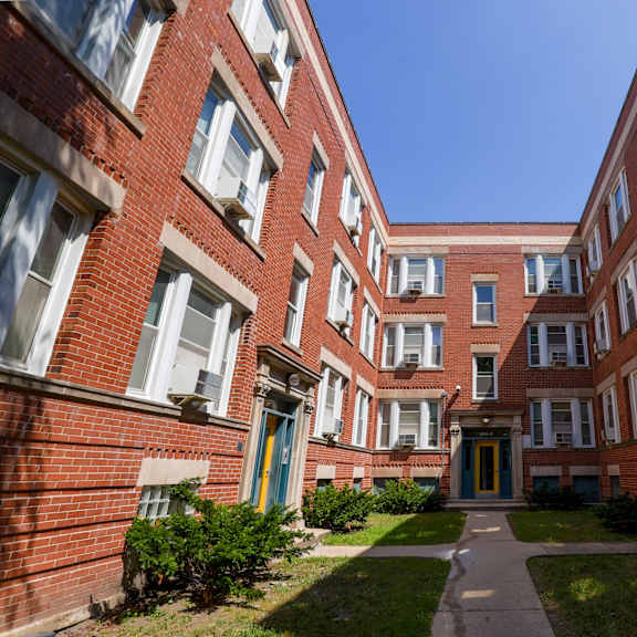 a long hallway with red brick buildings and green bushes on the side.