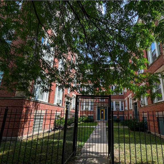 a black metal gate leads to a brick building with a green lawn.