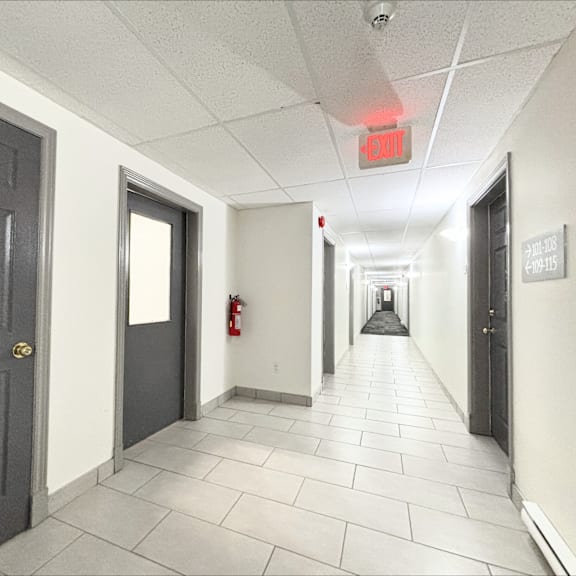 a long hallway with doors on either side and a red exit sign above.