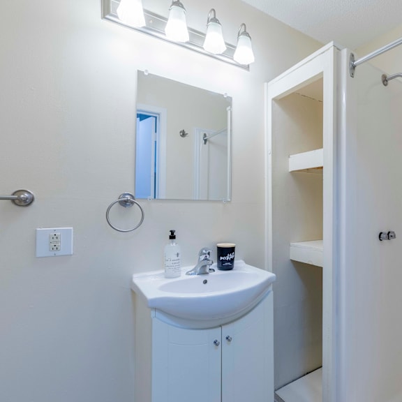 a white bathroom with a sink, mirror, and shower.