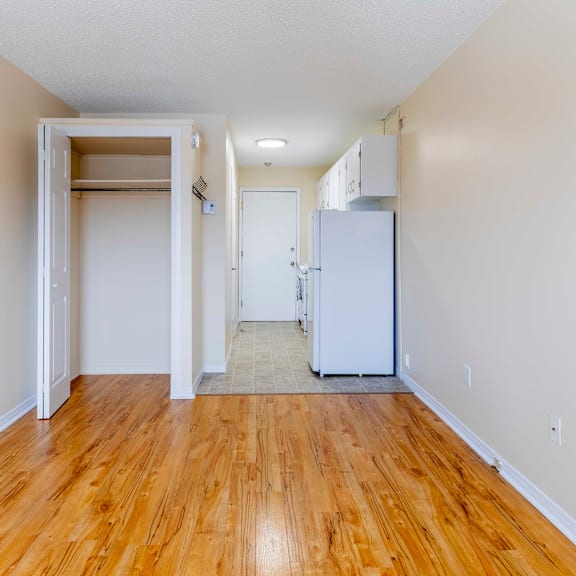 a room with a white fridge and wooden floors.