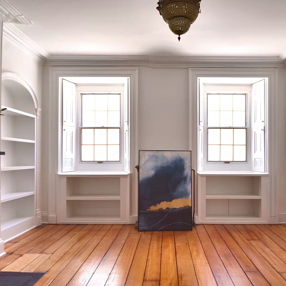 a room with a painting in the middle and two windows.