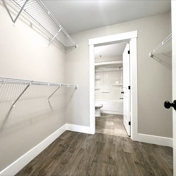 a white hallway with wood flooring and open doors leading to a bathroom.
