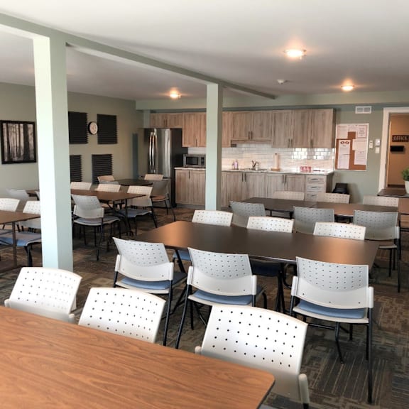 a cafeteria with tables and chairs and a kitchen in the background.