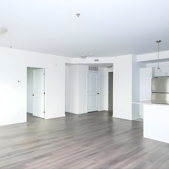 a white room with a wooden floor and a kitchen area in the background.