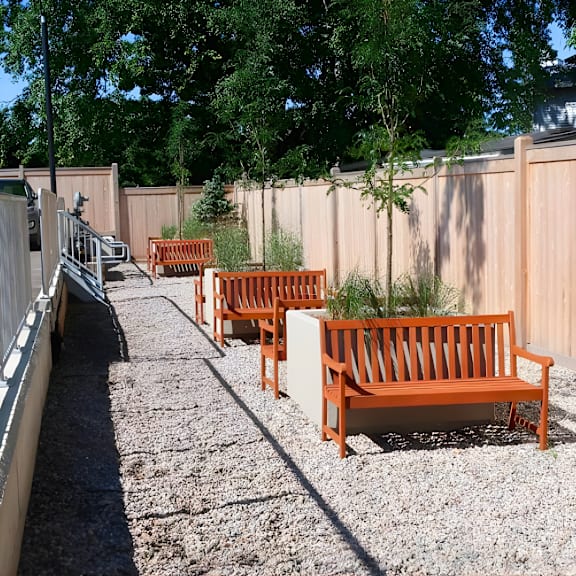 a row of orange benches are lined up on a gravel path.