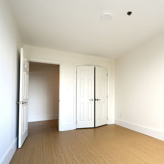 a room with white walls and wooden flooring with two white doors.