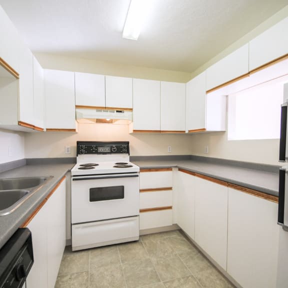 a white kitchen with a stove, sink, and cabinets.
