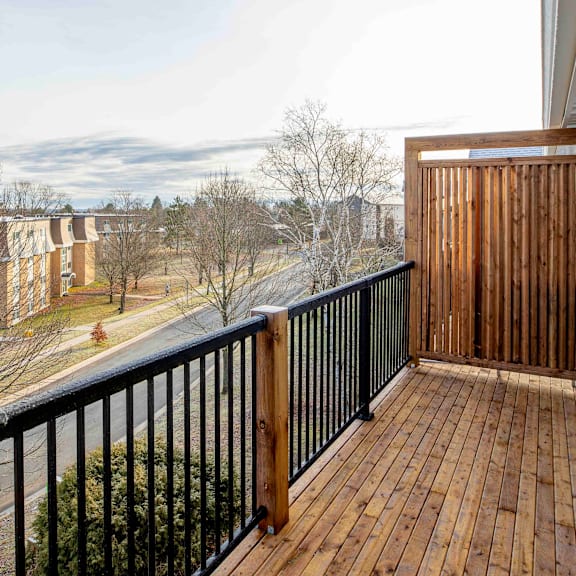 a balcony with a black railing and wooden floor overlooks a residential area.