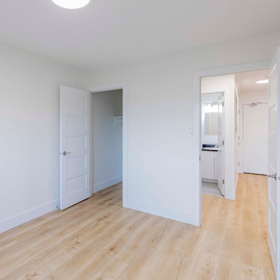 a room with white walls and wooden flooring with a door open to another room.